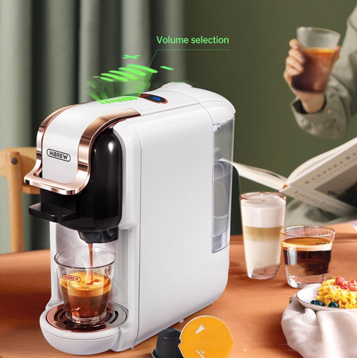 White coffee machine dispensing coffee into a glass on a wooden table with a person holding a cup in the background.