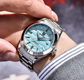 Person wearing a silver watch with a blue face on a blurred background