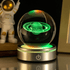 Glass sphere with glowing green Saturn model on a metallic base, with an astronaut figure in the background.