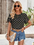 Woman wearing Amy Petal Sleeve Top with petal sleeves, black fabric, gold accents, paired with denim shorts.