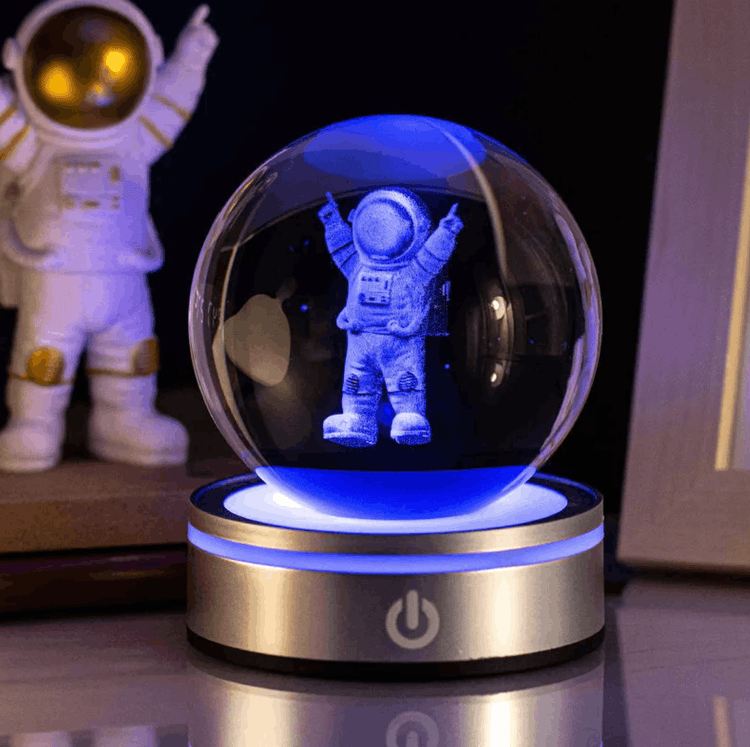Glass ball with an astronaut figure inside, illuminated by blue light, on a dark background.