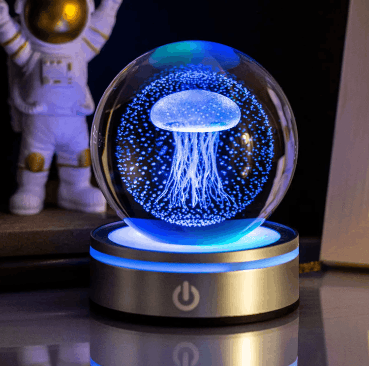 Glass orb with jellyfish design on a rotating base, illuminated by blue light, with an astronaut figure in the background.