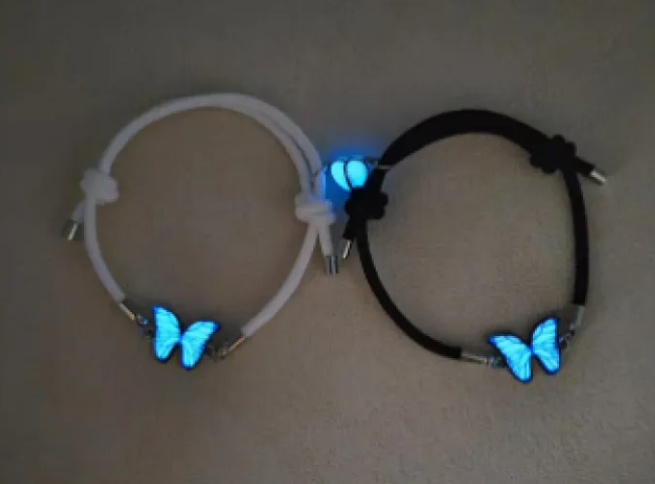 Two bracelets with butterfly charms glowing blue on a neutral background