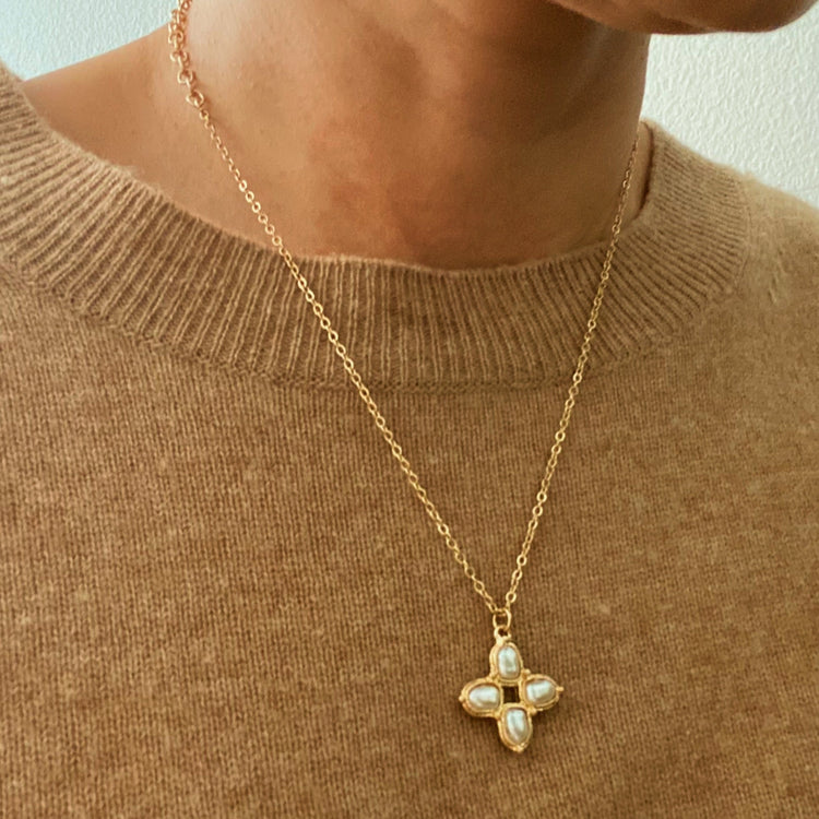 Gold necklace with a pendant worn by a person in a brown sweater.
