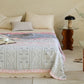 Bed with patterned quilt and pillows in a room with a side table and books.