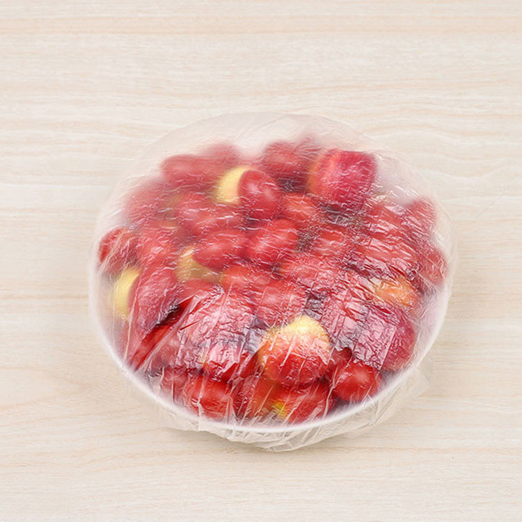 A clear plastic wrap lid covering a bowl of red dates, placed on a light beige wood-grain surface.