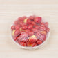 A clear plastic wrap lid covering a bowl of red dates, placed on a light beige wood-grain surface.