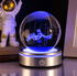 Crystal ball with 3D astronaut figure inside, illuminated by blue light, on a dark background.
