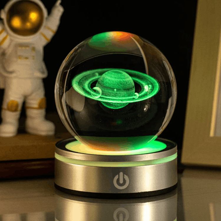 Glass sphere with glowing green Saturn model on a metallic base, with an astronaut figure in the background.