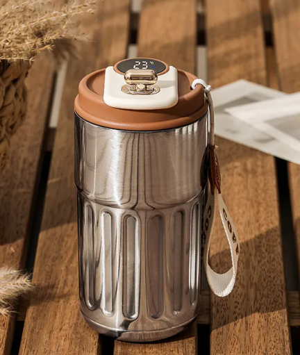 Stainless steel tumbler with brown lid on a wooden surface