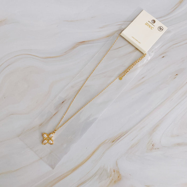 Gold necklace with a clover pendant on a marble surface