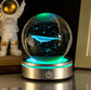 Glass ball with a whale inside, illuminated by green light, on a reflective surface.