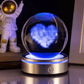 Glass sphere with blue heart light inside, placed on a reflective surface with an astronaut figure in the background.